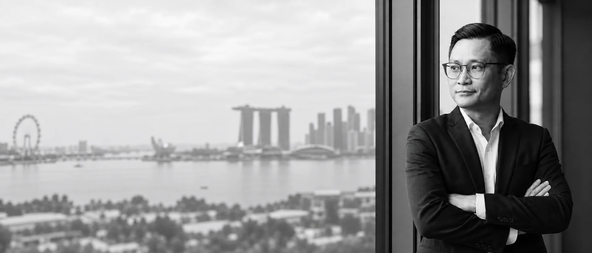 Ziqian, arms folded, Marina Bay skyline in soft bokeh behind him, black and white editorial portrait
